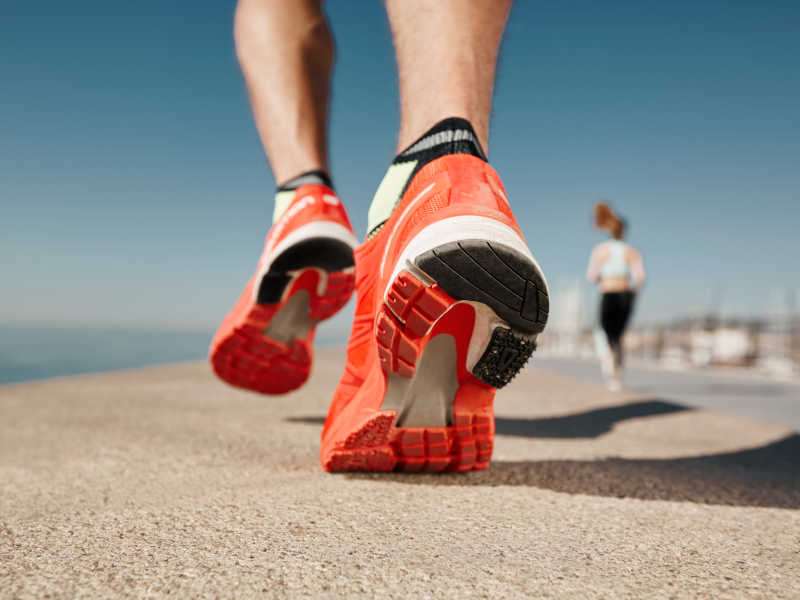 Close up of the orange running shoes of a jogger who is running outside near a beach.
