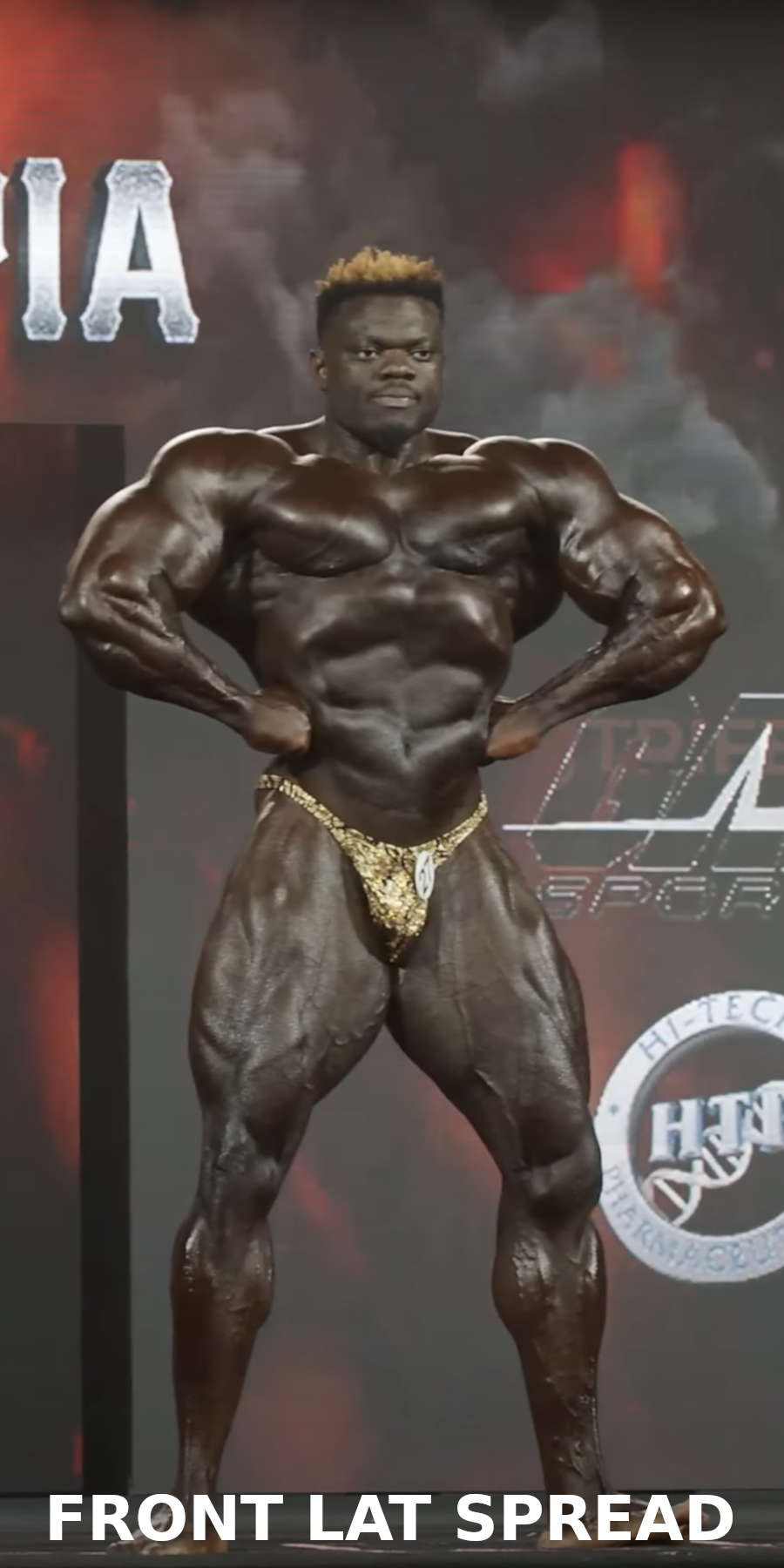 A bodybuilder performing the front lat spread pose on stage during a bodybuilding competition 