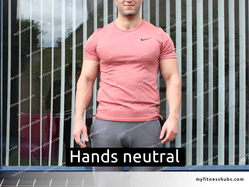 A fit man wearing workout clothing while standing outside in front of a window, with his hands in a neutral position.