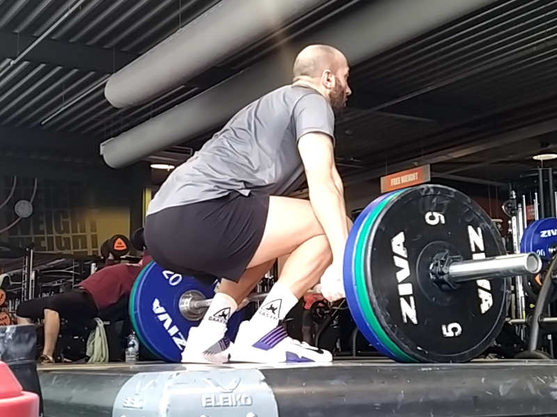 A man with workout clothes on standing on a deadlifting platform in a starting position to do a deadlift.