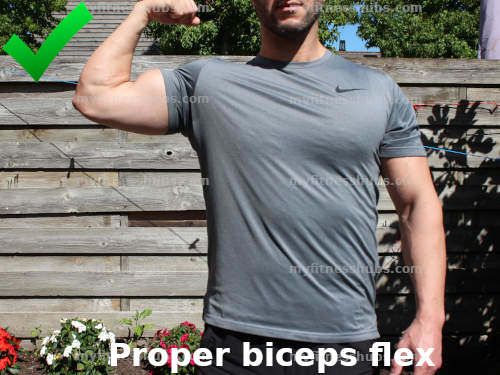 A front, close-up view of a fit doing a proper biceps flex while standing outside and wearing workout clothing.