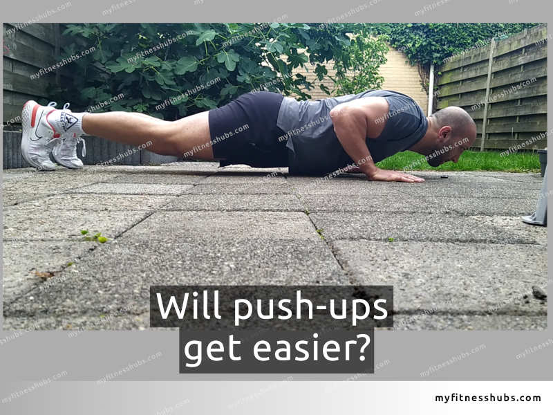 A fit, male athlete wearing workout clothing doing a push-up in a small backyard.