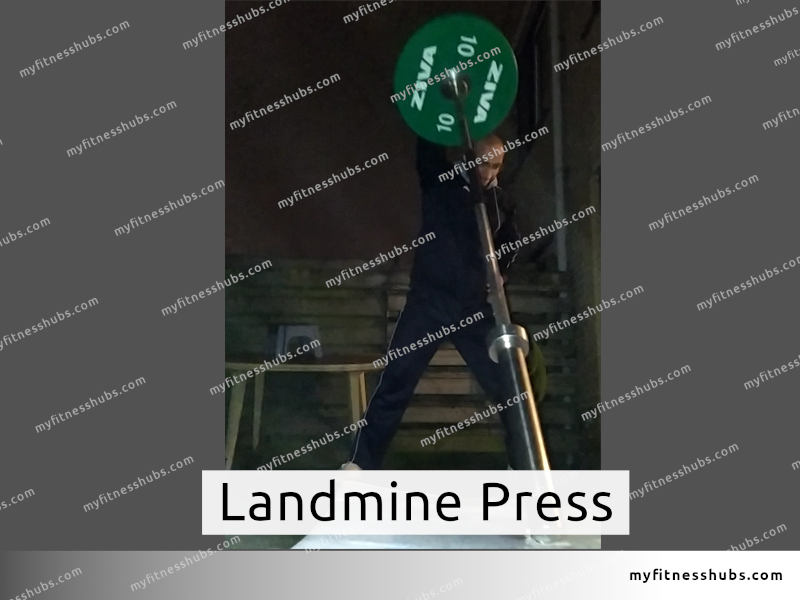 A fit man wearing workout clothes doing the Landmine press outdoor in a garden during a cold night in winter.