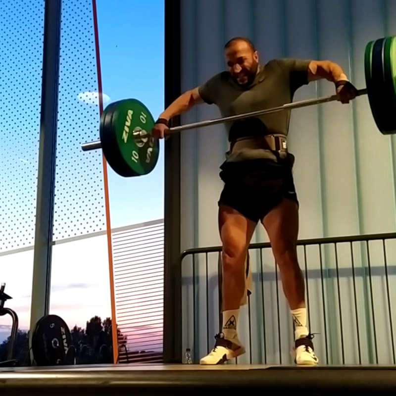 A man doing snatch high pulls on a deadlift platform in the gym while wearing a lifting belt.