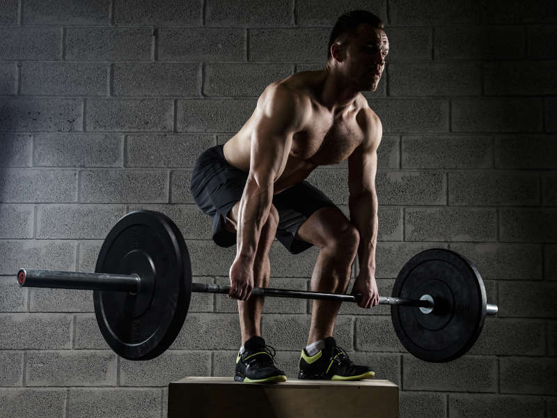 A man holding a barbell and performing the deadlift exercise.
