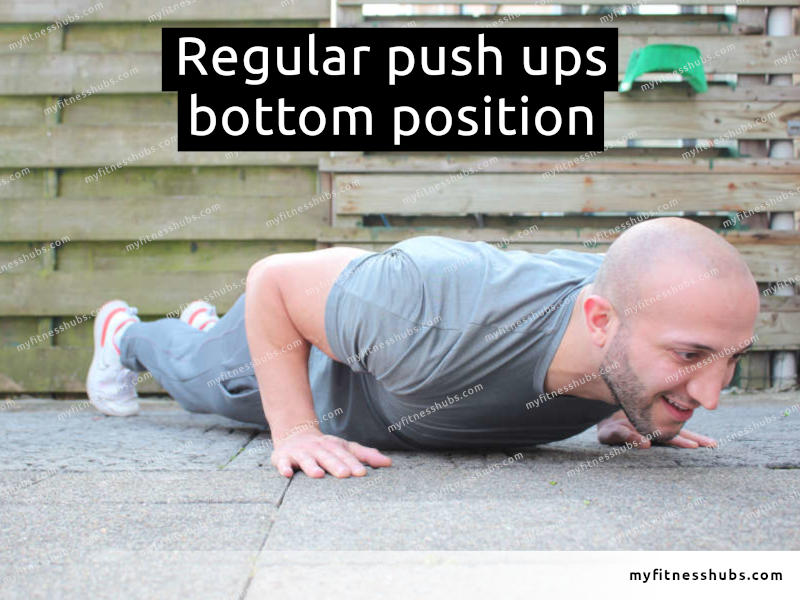 A view of a front angle view of an athletic man in the bottom position of a push up done outdoors.