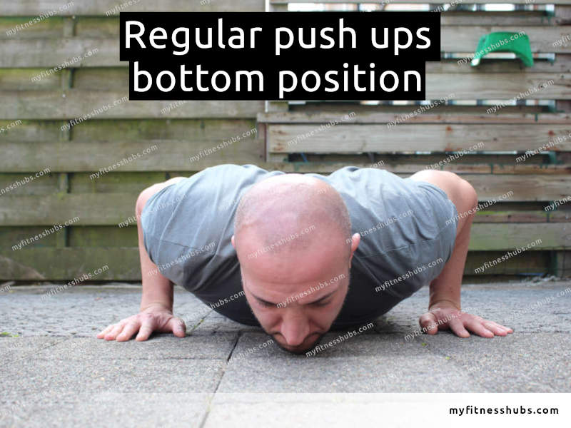 A front view of an athletic man in the bottom position of a push up done outdoors.