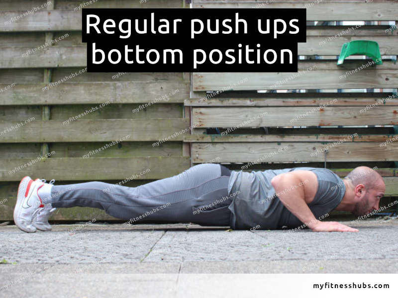 A side view of an athletic man in the bottom position of a push up done outdoors.