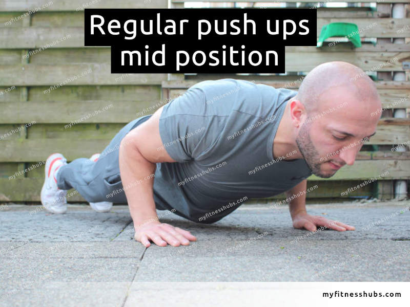 A view of a front angle view of an athletic man in the middle position of a push up done outdoors.