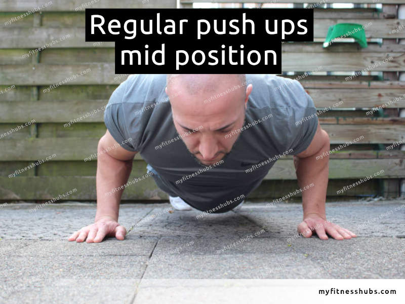 A front view of an athletic man in the middle position of a push up done outdoors.