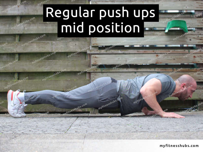 A side view of an athletic man in the middle position of a push up done outdoors.