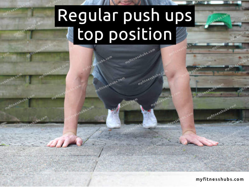 A front view of an athletic man in the top position of a push up done outdoors.