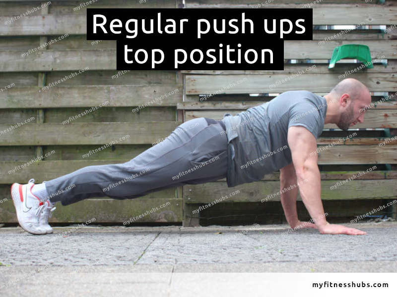 A side view of an athletic man in the top position of a push up done outdoors.