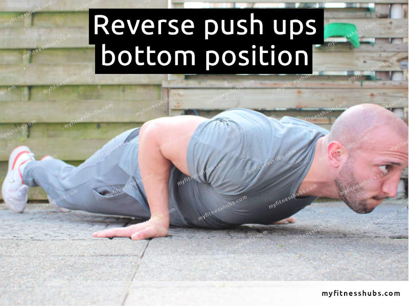 A view of a front angle view of an athletic man in the bottom position of a reverse push up done outdoors.