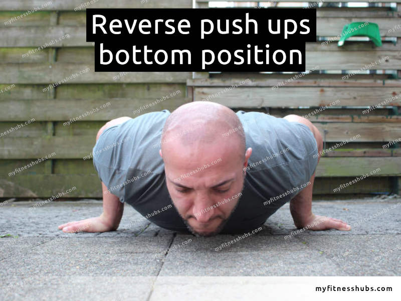 A front view of an athletic man in the bottom position of a reverse push up done outdoors.