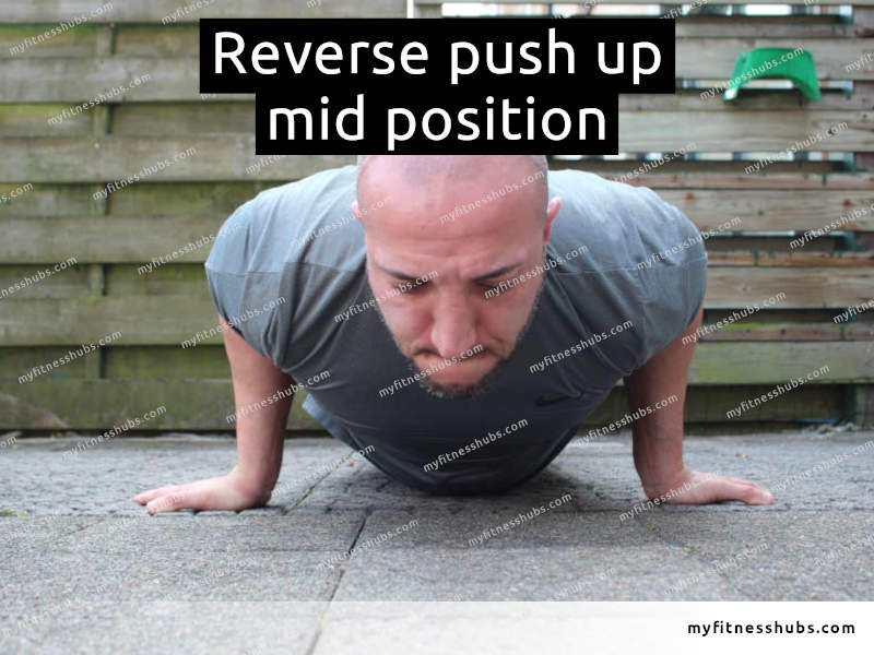 A front view of an athletic man in the middle position of a reverse push up done outdoors.