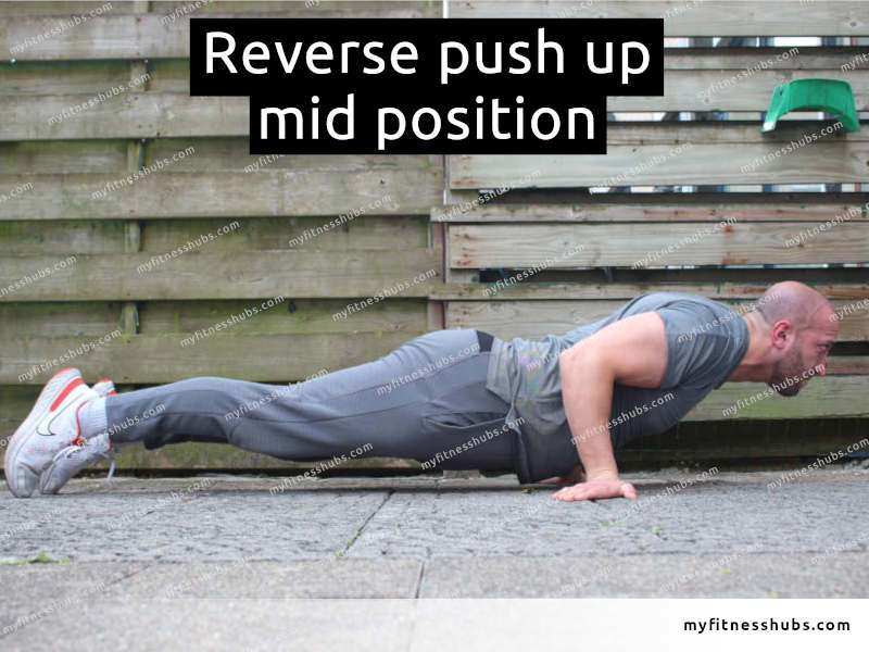 A side view of an athletic man in the middle position of a reverse push up done outdoors.