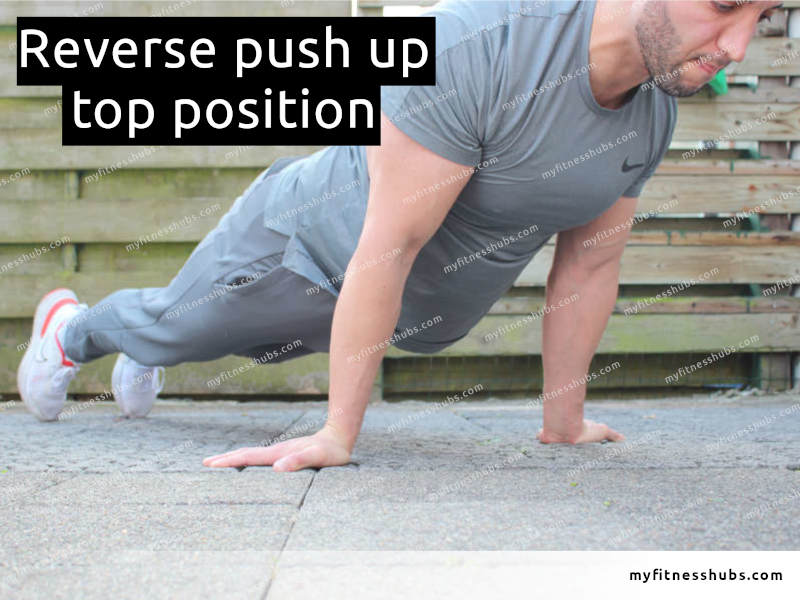 A view of a front angle view of an athletic man in the top position of a reverse push up done outdoors.
