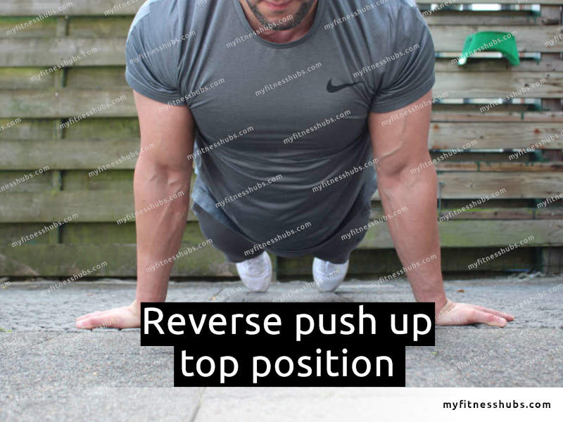 A front view of an athletic man in the top position of a reverse push up done outdoors.