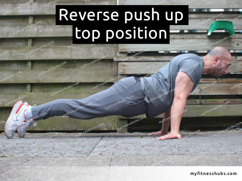 A side view of an athletic man in the top position of a reverse push up done outdoors.